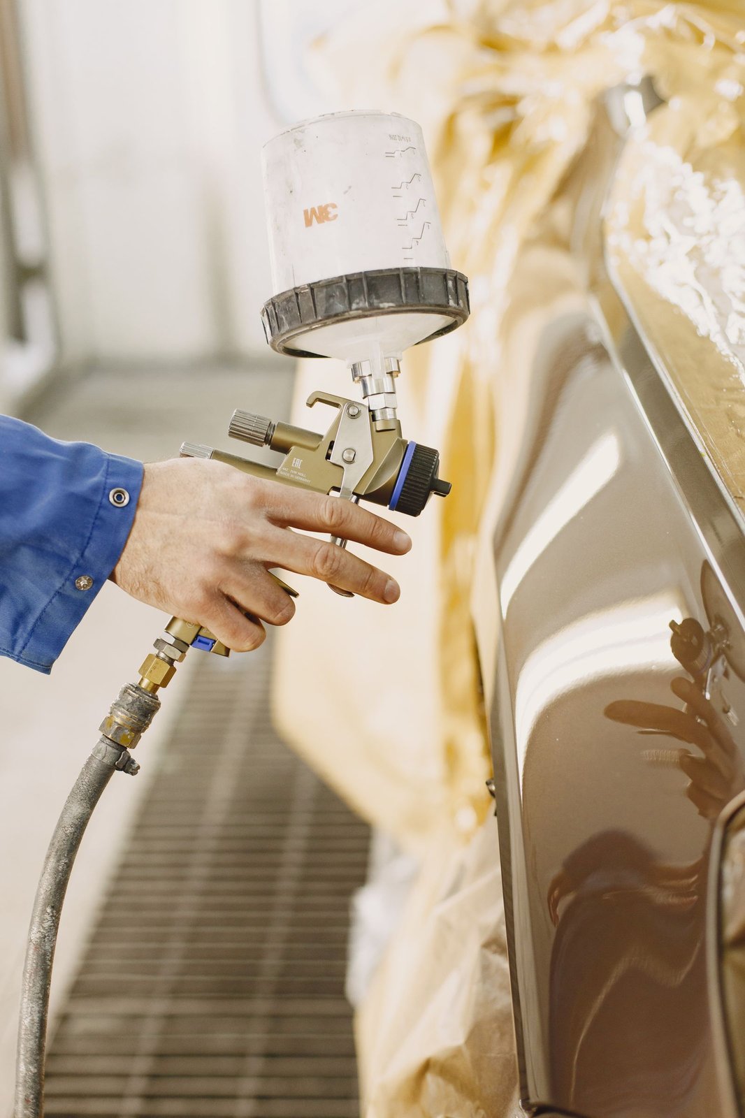 Técnico aplicando pintura automotiva com pistola em cabine de pintura